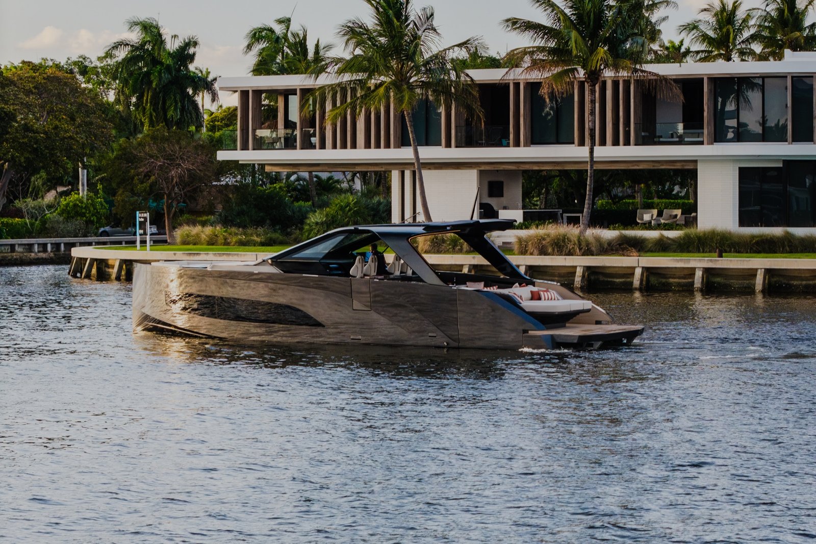 A dark motor yacht cruising past a modern waterfront residence